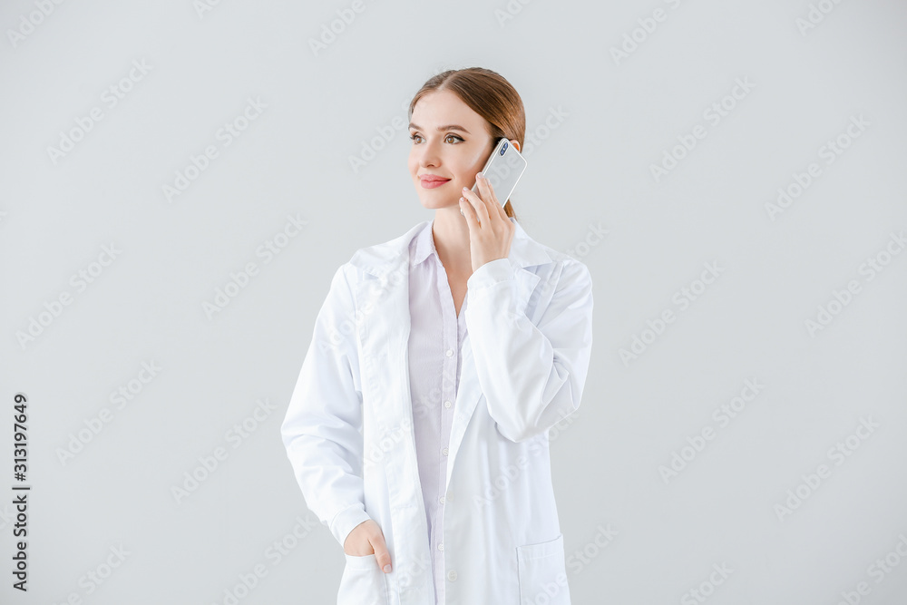 Portrait of female doctor talking by mobile phone on light background Portrait of female doctor talking by mobile phone on light background