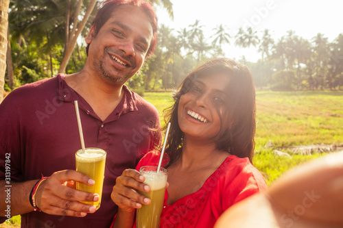 happy indian family holding glass of fresh cane juice with eco metal tube and taking selfie portrait photo on camera smartphone. travel and save planet recyclable concept