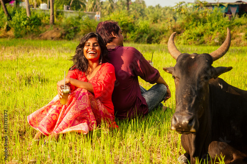 happy indian couple in love sitting on field near cow,drinking cane juice in Goa farm