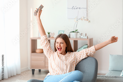 Happy woman watching TV while sitting in armchair at home