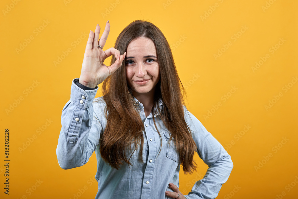 Cheerful charming caucasian woman wearing fashion shirt isolated on orange background in studio doing okay gesture, smiling. People emotions, lifestyle concept. Cheerful charming caucasian woman wearing fashion shirt isolated on orange background in studio doing okay gesture, smiling. People emotions, lifestyle concept.