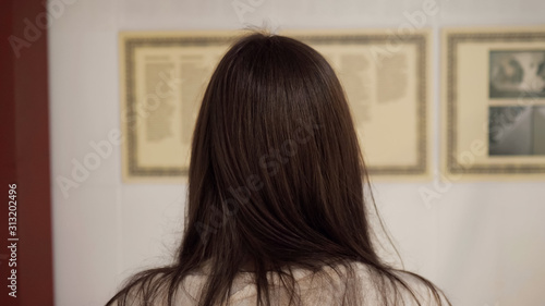 brunette lady with long hair stands in national art gallery and reads introductory information close backside view