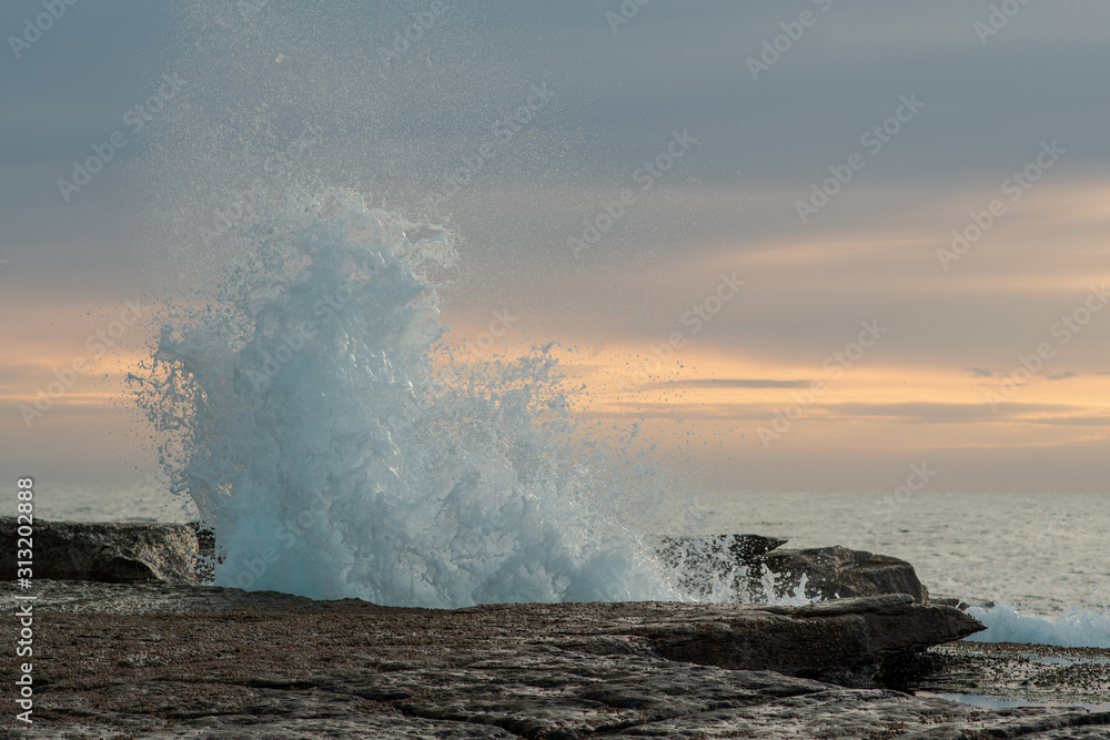 Fototapeta premium Waves crashing against rocks with sunrise in the background