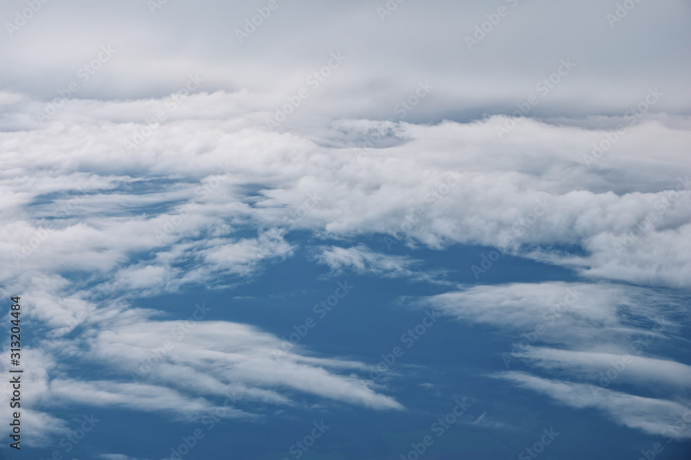 Aerial view from the airplane. Flying over the layer of clouds and looking on landscape through the clouds. Soft sunlight in sky. Aerial view from the airplane. Flying over the layer of clouds and looking on landscape through the clouds. Soft sunlight in sky.