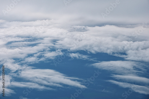 Fototapeta Naklejka Na Ścianę i Meble -  Aerial view from the airplane. Flying over the layer of clouds and looking on landscape through the clouds. Soft sunlight in sky.