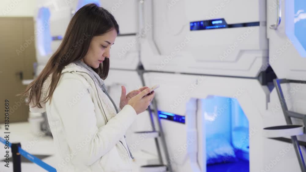 Young woman uses phone to pay online for sleeping capsules at airport Young woman uses phone to pay online for sleeping capsules at airport