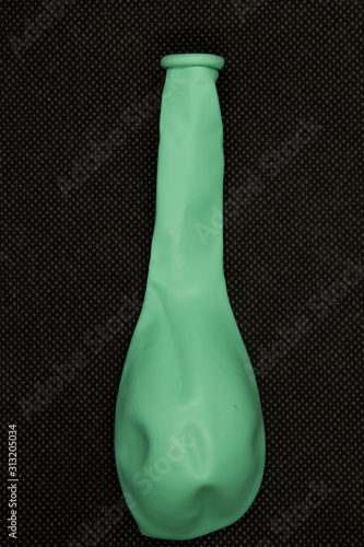 This is a photograph of a Green deflated balloon isolated on a textured Black background
