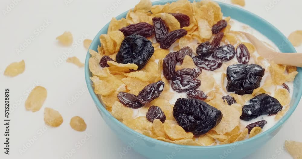 Truck shot of Cornflakes prunes and resin with milk and wooden spoon in the blue bowl on white background Truck shot of Cornflakes prunes and resin with milk and wooden spoon in the blue bowl on white background