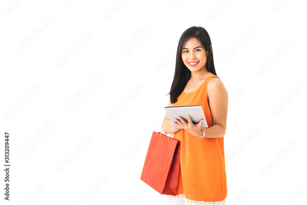 A beautiful Asian young woman wearing orange dress holding shopping bag and a tablet in front of white isolated background. A beautiful Asian young woman wearing orange dress holding shopping bag and a tablet in front of white isolated background.