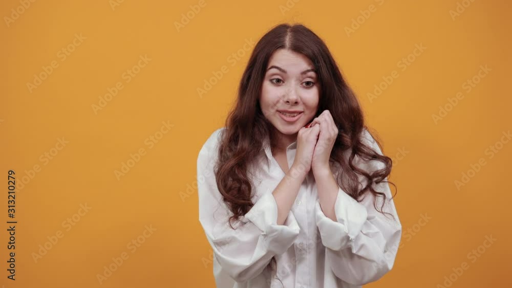 Cheerful caucasian young woman in fashion white shirt keeping hands on cheek, smiling, looking at camera isolated on orange background in studio. People sincere emotions, lifestyle concept. Cheerful caucasian young woman in fashion white shirt keeping hands on cheek, smiling, looking at camera isolated on orange background in studio. People sincere emotions, lifestyle concept.