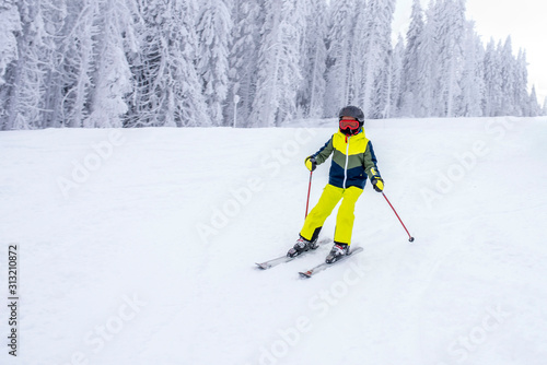 Child in ski suit skiing downhill in high mountains during winter season
