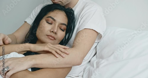 Close up of lover sitting in bed thinking about future. Caucasian male with his girlfriend, asian woman in black lingerie. Happy lover in bed concept. photo