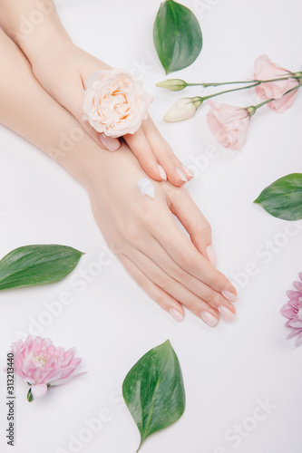 Fototapeta Naklejka Na Ścianę i Meble -  Top view cosmetic cream on female hands with pink flowers on white background, flat lay. Concept spa skin care