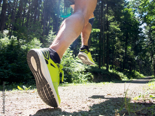 Male runner running on road through forest. Focus on leg.