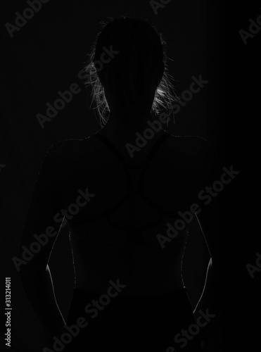 Fototapeta Naklejka Na Ścianę i Meble -  Schwarz-weiß Umrisse des Körpers einer Frau mit Haaren im Dunkeln und Hintergrundbeleuchtung
