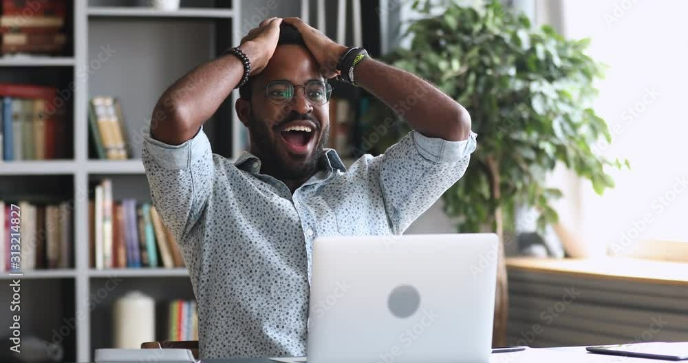 Amazed young african man read great news online on laptop