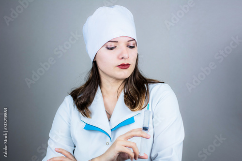 doctor woman in white coat with dark hair in medical blue mask holds syringe in hands on light background photo