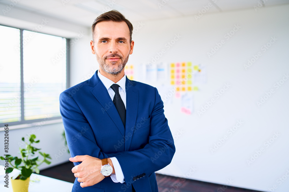 Shot of positive mature businessman standing in modern office with crossed arms Shot of positive mature businessman standing in modern office with crossed arms