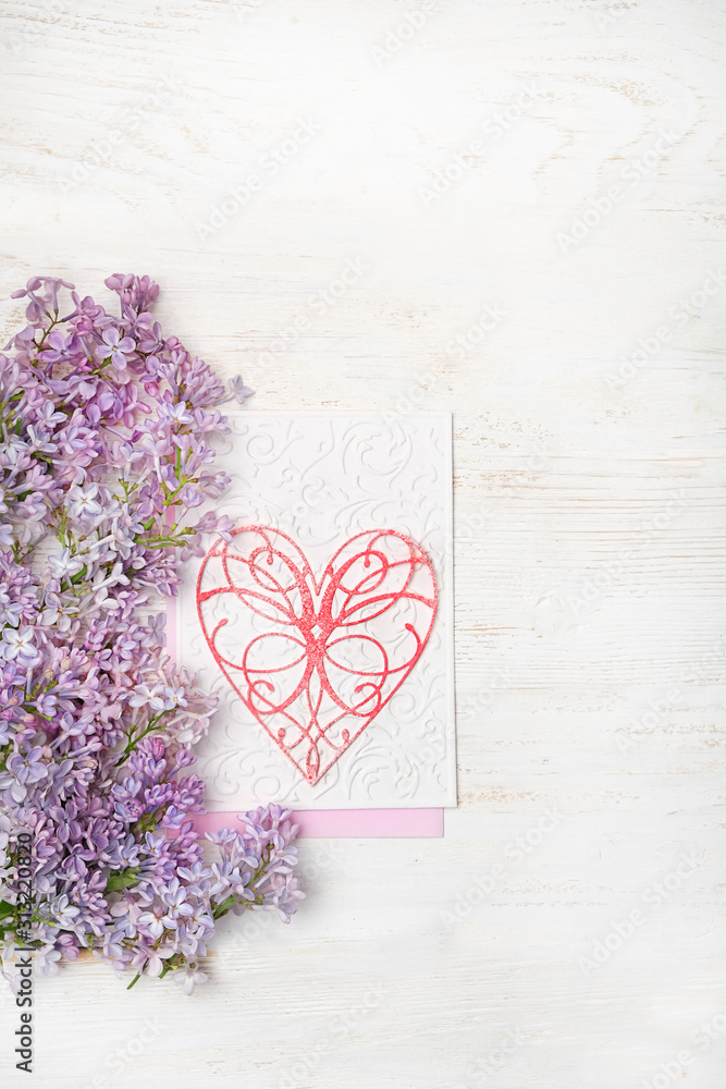 Fototapeta premium Background with lilac flowers and decorative heart on white wooden table. Concept for Valentine's Day, Happy Mothers Day Greetings card. copy space