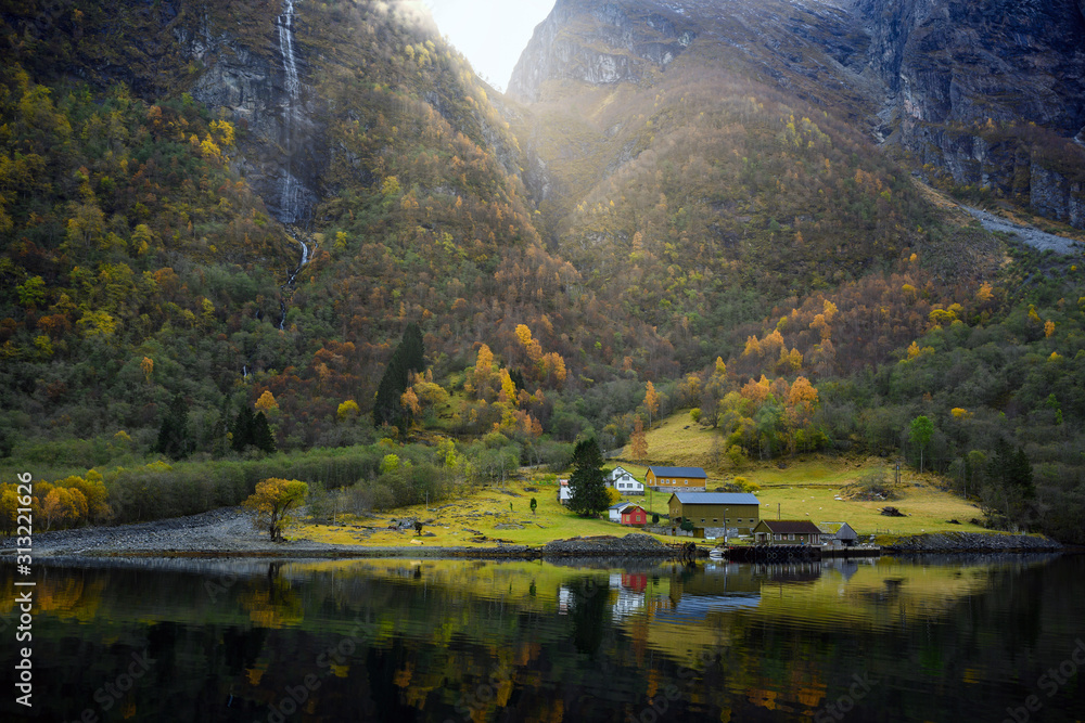 Small village on the waterfront and mountains in the autumn season that reflect the water. Watch from a boat trip to see the beauty of Sognefjord Cruise, program from Gudvangen to Flam in Norway.