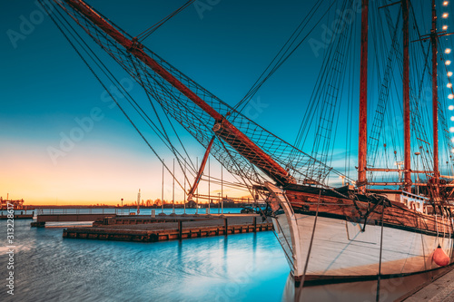 Helsinki, Finland. Old Wooden Sailing Vessel Ship Schooner Is Moored To City Pier, Jetty. Lighting At Evening Or Night Illumination