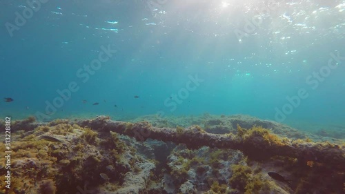 Rocky seabed illuminated by the rays of the sun and a communication cable in a pipe at the bottom of the sea. Underwater shooting.