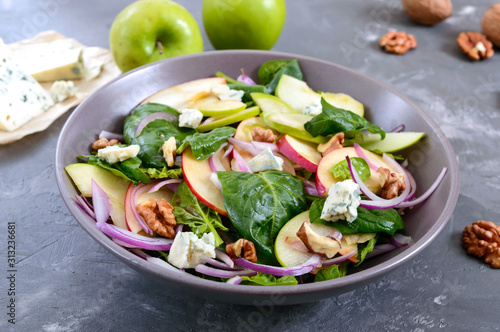 Tasty diet fitness salad with spinach, apples, red onions, blue cheese, nuts. Proper nutrition. Light concrete background