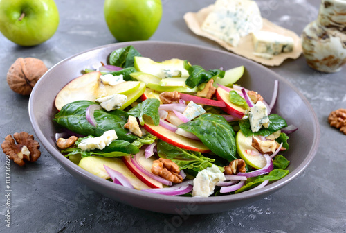 Tasty diet fitness salad with spinach, apples, red onions, blue cheese, nuts. Proper nutrition. Light concrete background