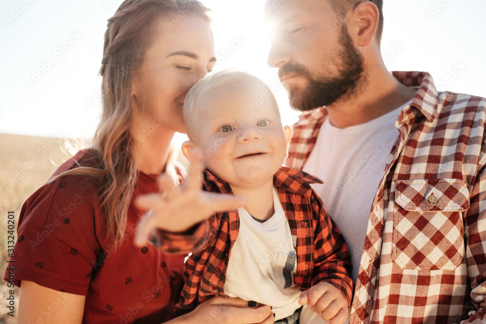 Happy Young Family Mom and Dad with Their Little Son Enjoying Summer Weekend Picnic Outside the City in the Field at Sunny Day Sunset, Vacation Time Concept Happy Young Family Mom and Dad with Their Little Son Enjoying Summer Weekend Picnic Outside the City in the Field at Sunny Day Sunset, Vacation Time Concept