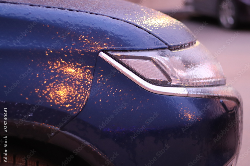 Icing a car in winter. Front part of a car with headlights close-up