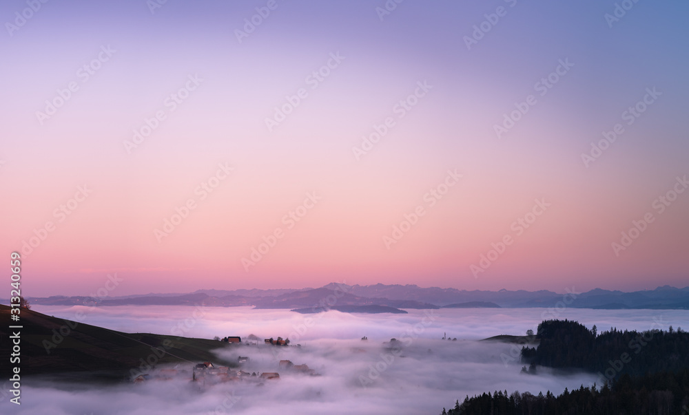 panoramic view of a village in switzerland covered in fog after the sunset with warm colors