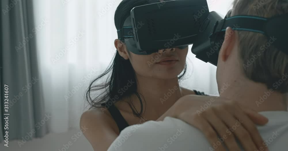 Close up of lover using virtual reality trying to have sex in bed, close up of face smile. Caucasian male with his girlfriend in black mask, asian woman in black lingerie. Future cyber sex concept. Close up of lover using virtual reality trying to have sex in bed, close up of face smile. Caucasian male with his girlfriend in black mask, asian woman in black lingerie. Future cyber sex concept.
