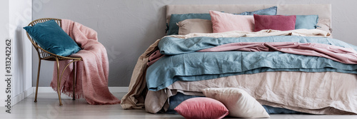 Trendy golden chair with pastel pink blanket and blue pillow next to big comfortable bed photo