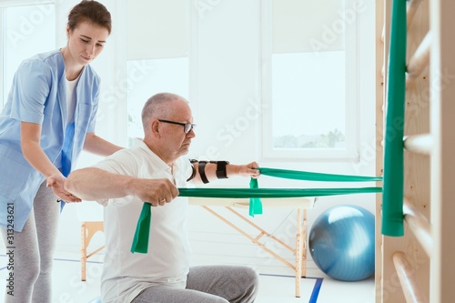 Elderly man doing gymnastic exercises with a young female physiotherapist