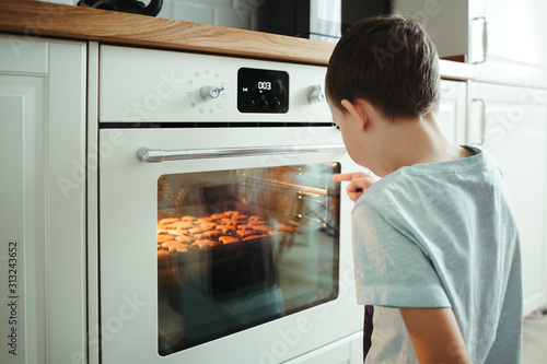 Tablou canvas A young boy cooks cookies and patiently waiting next to a safe oven in the home interior