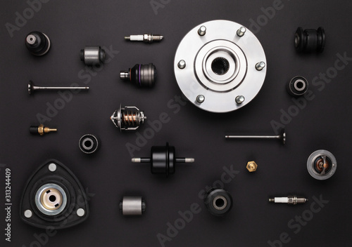 Studio photography - a lot of automotive parts: valves, spark plugs, silent blocks, thermostats,  sensors, wheel hub, bearings, lie in straight rows on a flat surface isolated on a black background.