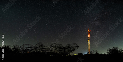 Antenna array of radio astronomy telescope on background with night sky and TV-tower