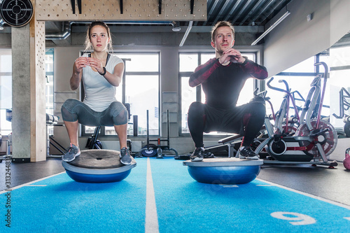 Fit couple working on bosu ball in fitness studio. Doing a squat exercise photo