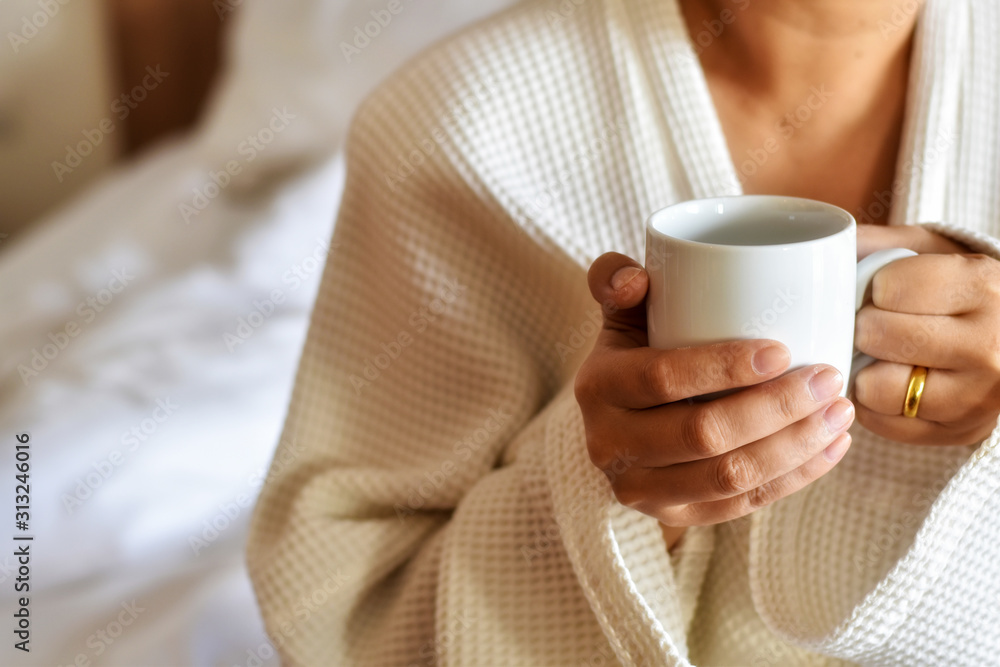 Woman in bathrobe, A white coffee mug in holding hand of a woman.