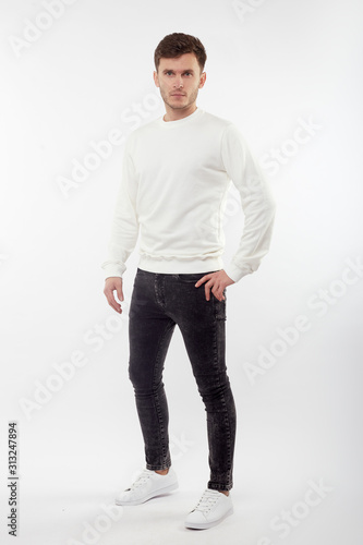 Young european man in white sweater and black pants posing on white background. Isolated.