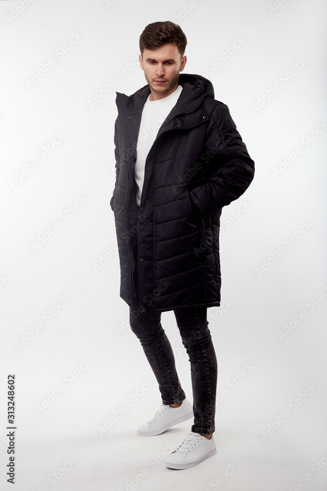 Young european man in white sweater and black pants, black down jacket posing on white background. Isolated. Young european man in white sweater and black pants, black down jacket posing on white background. Isolated.