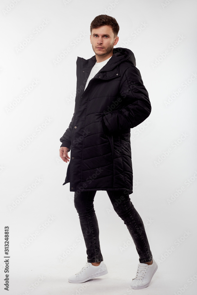 Young european man in white sweater and black pants, black down jacket posing on white background. Isolated. Young european man in white sweater and black pants, black down jacket posing on white background. Isolated.