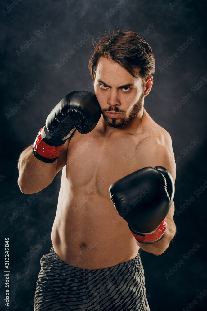 shirtless boxer with gloves on dark background in smoke