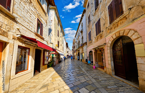 Fototapeta Croatia Porec. Central street old town paved stone paving stones with storefront shop in vintage house and windows with shutters. Sunny day and blue sky with white clouds.