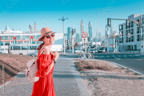 A tourist girl with a backpack walks on the sidewalk near a busy street in Dubai © EdNurg