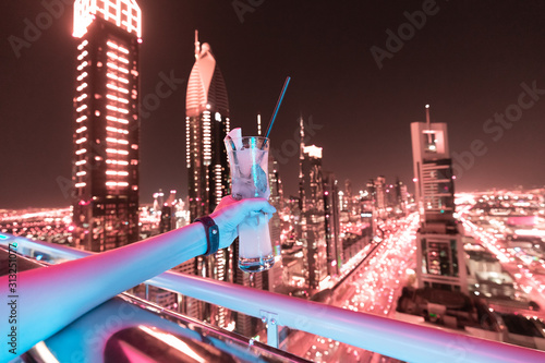 Photography drinking cocktail in a rooftop nightclub bar with night cityscape at the backgro