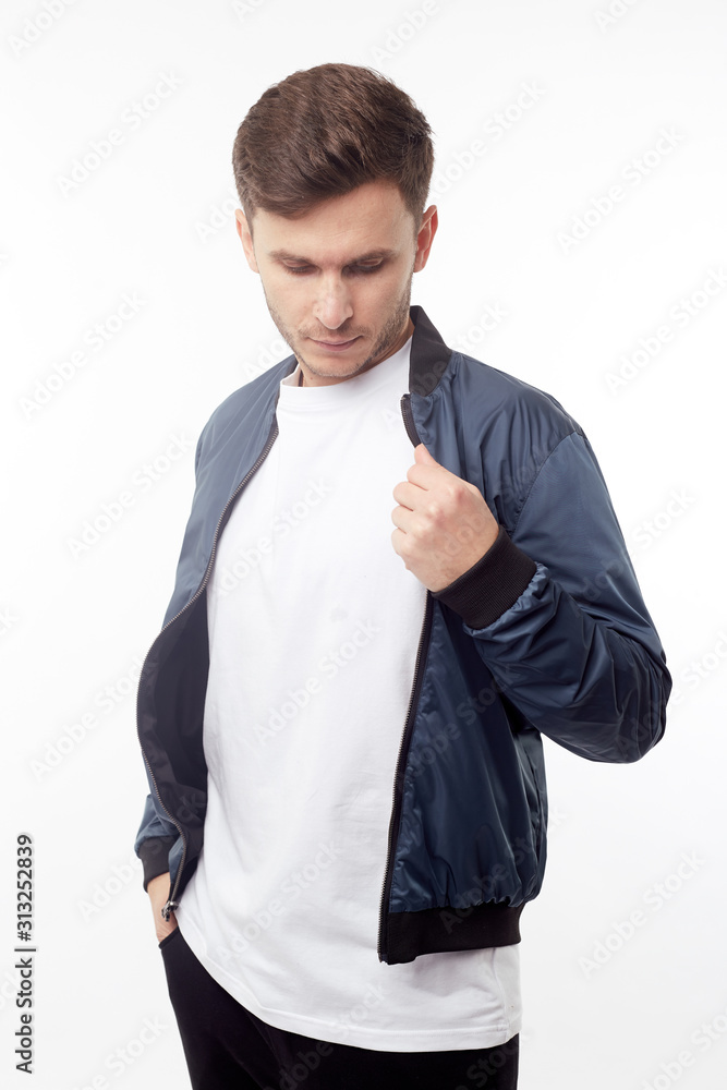 Young european man in white sweater and black pants, blue bomber jacket posing on white background. Isolated. Young european man in white sweater and black pants, blue bomber jacket posing on white background. Isolated.