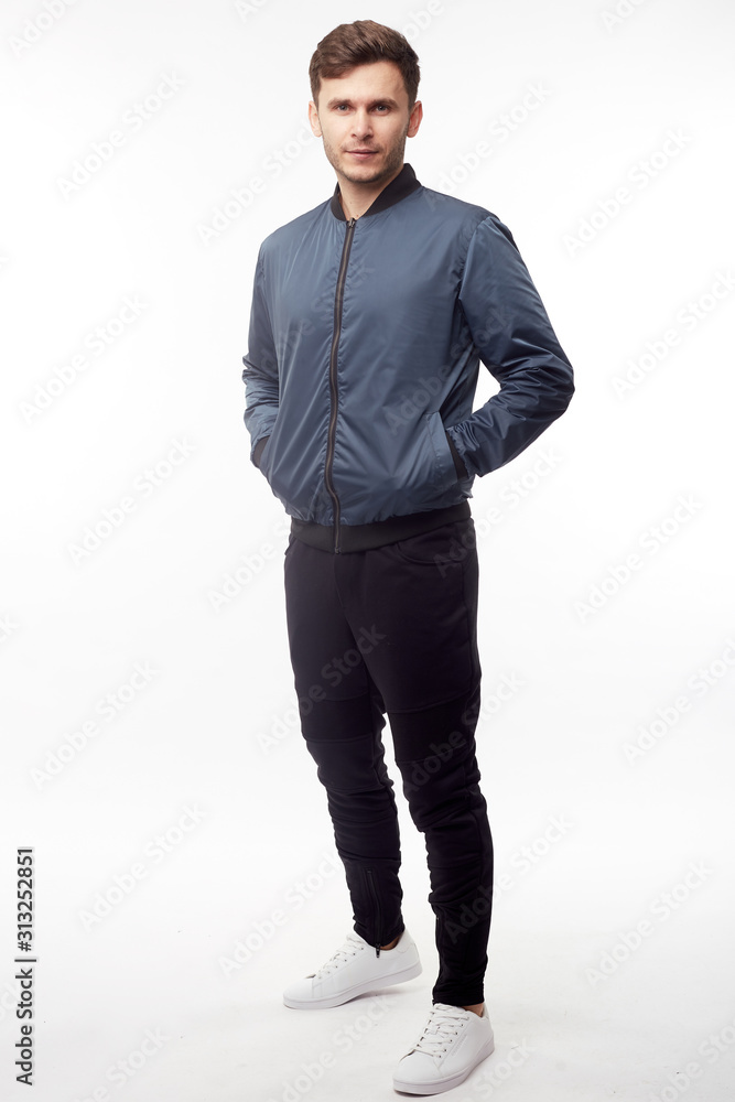 Young european man in white sweater and black pants, blue bomber jacket posing on white background. Isolated. Young european man in white sweater and black pants, blue bomber jacket posing on white background. Isolated.