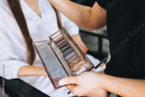 Girl professional makeup artist is holding a palette of shadows, a palette. Cosmetics with multi-colored eyeshadows close-up. Photography, concept.