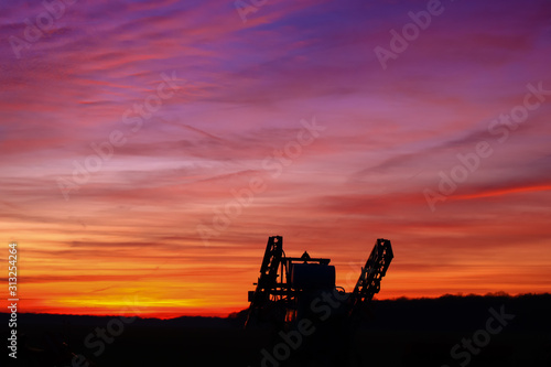 Incredible very colorful sunset in the countryside. Silhouette of an industrial agricultural machine against the day. Cumulonimbus and stratus in a beautiful sky at night.